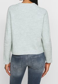 Ljusgrön stickad tröja med kort design, rund halsringning och långa raglanärmar. Kombinerad med blekta blåa skinny jeans.