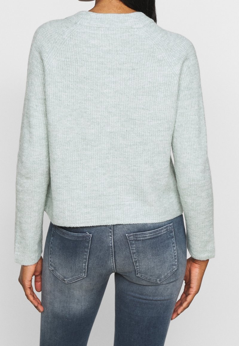 Ljusgrön stickad tröja med kort design, rund halsringning och långa raglanärmar. Kombinerad med blekta blåa skinny jeans.