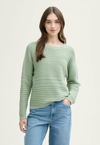 Suéter de rayas verde claro con escote redondo y mangas largas, combinado con jeans azules. La textura presenta un canalé horizontal.