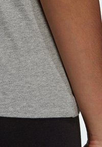 Jasnoszara koszulka z gładką teksturą, krótkimi rękawami i prostym dołem. Nosi się ją z czarnymi legginsami; materiał wydaje się miękki i elastyczny.