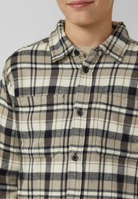 Knopenoverhemd met ruitpatroon in beige en zwart met tan-accenten. Gemaakt van flanel, met een kraag en twee borstzakken.