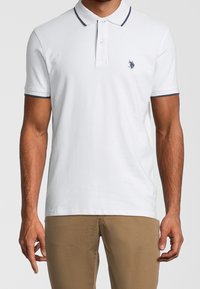 Vit kortärmad polo skjorta i bomull, med marinblå krage och ärmdetaljer, samt en liten broderad logotyp på vänster bröst.