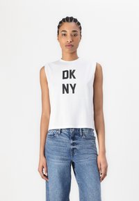 Fehér ujjatlan cropped top, középen merész fekete "DKNY" felirattal; világoskék, magas derekú farmernadrággal párosítva.
