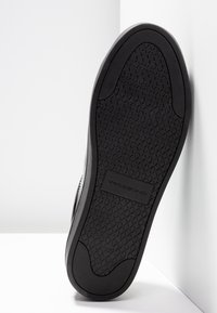 Semelle noire de sneaker avec motif en losanges, nom de marque « Vagabond » embossé au centre, taille 37, inclinée sur un fond d’angle blanc.