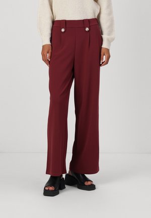 Bordeaux wijde broek met een gladde stof, voorzien van een hoge taille, dubbele knoopaccenten en een getailleerde pasvorm. Gecombineerd met zwarte sandalen met blokhak.