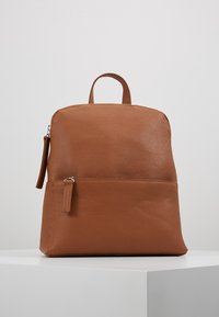 Sac à dos en cuir marron avec une surface texturée, forme arrondie, poignée supérieure, fermeture éclair, et une poche avant avec détail de fermeture éclair.