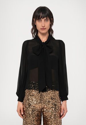Blusa negra transparente con un gran cuello de lazo, mangas largas abullonadas, combinada con pantalones de lentejuelas en color rosa dorado. Textura suave y diseño ajustado.