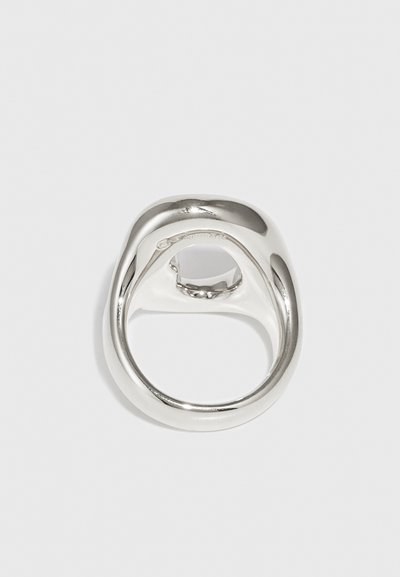 Anello in metallo argentato, liscio, con un design rotondo e scultoreo e un dettaglio a intaglio sulla parte superiore. Superficie riflettente senza pattern visibili.