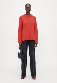Maglione rosso a maglia con orlo a costine, abbinato a pantaloni neri a gamba larga e una piccola borsa nera con dettagli in borchie.