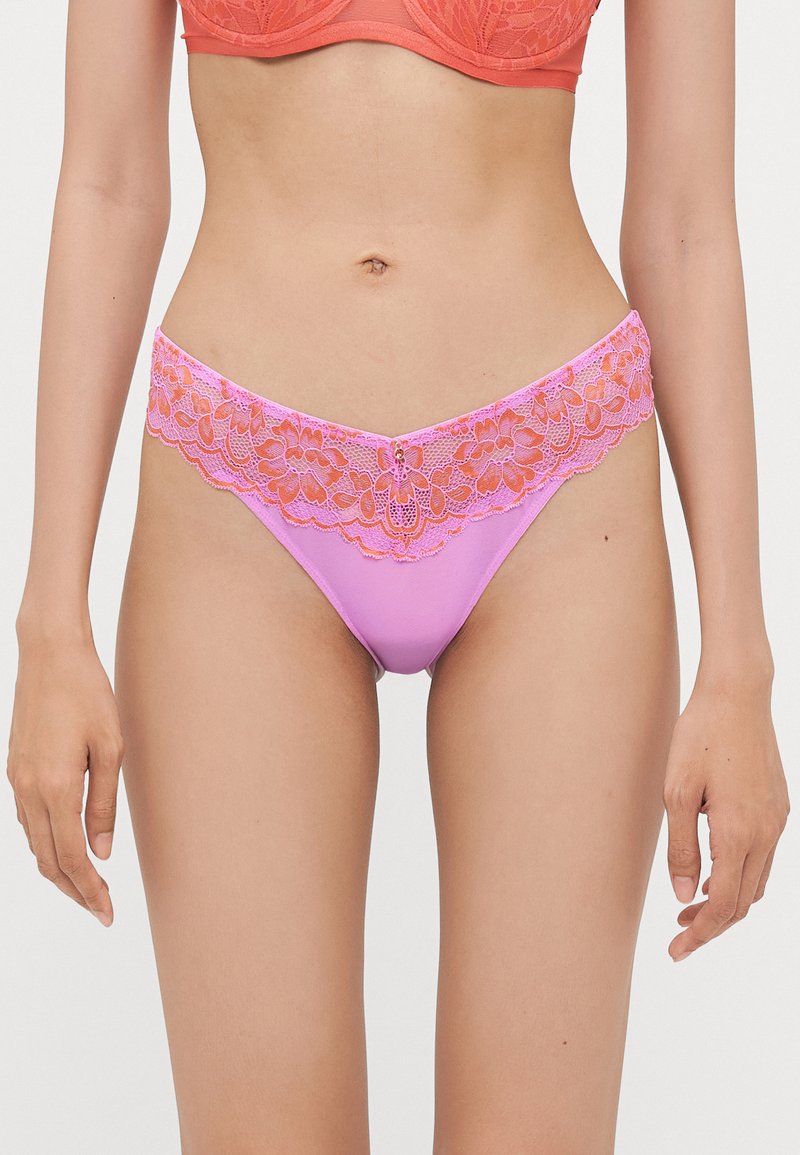 Roze onderbroek met kantafwerking heeft een bloemenpatroon op de tailleband en een glad, effen roze lichaam. Het ontwerp is laag op de heupen en aansluitend.