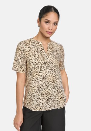 Short-sleeve blouse made of lightweight fabric in beige with black scattered pattern. Features a V-neckline and a relaxed fit.