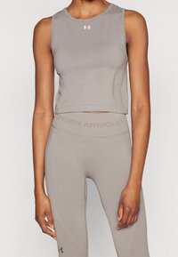 Šedý elastický krátký top s kulatým výstřihem a logem na prsou, ve spojení s ladícími legínami s vysokým pasem a textem značky.