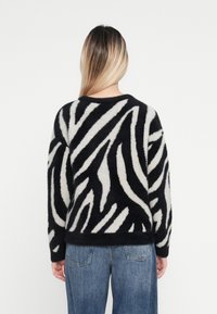 Uldne sort-hvide zebra-mønstrede sweater med rund hals, lange ærmer og afslappet pasform, parret med lyseblå denimjeans.