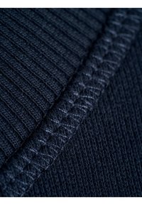 Navyblaues geripptes Gewebe mit einer strukturierten Oberfläche. Eine kontrastierende Naht zeigt komplizierte Details entlang der Kante.