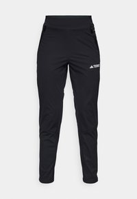 Pantalons de sport noirs en tissu lisse, avec un design ajusté, des poches zippées et une texture au bas des jambes. Logo imprimé sur l'avant.