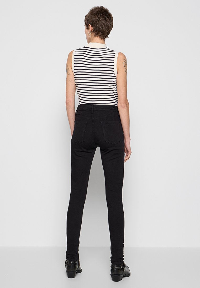 Schwarze enge Jeans mit hoher Taille, aus dehnbarem Denim, mit Gesäßtaschen und klassischem Design. Kombiniert mit einem gestreiften ärmellosen Oberteil.