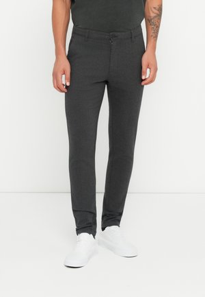 Pantalones de vestir gris oscuro, confeccionados en un tejido texturizado, con un diseño ajustado y cierre delantero de botón, combinados con unas zapatillas blancas.
