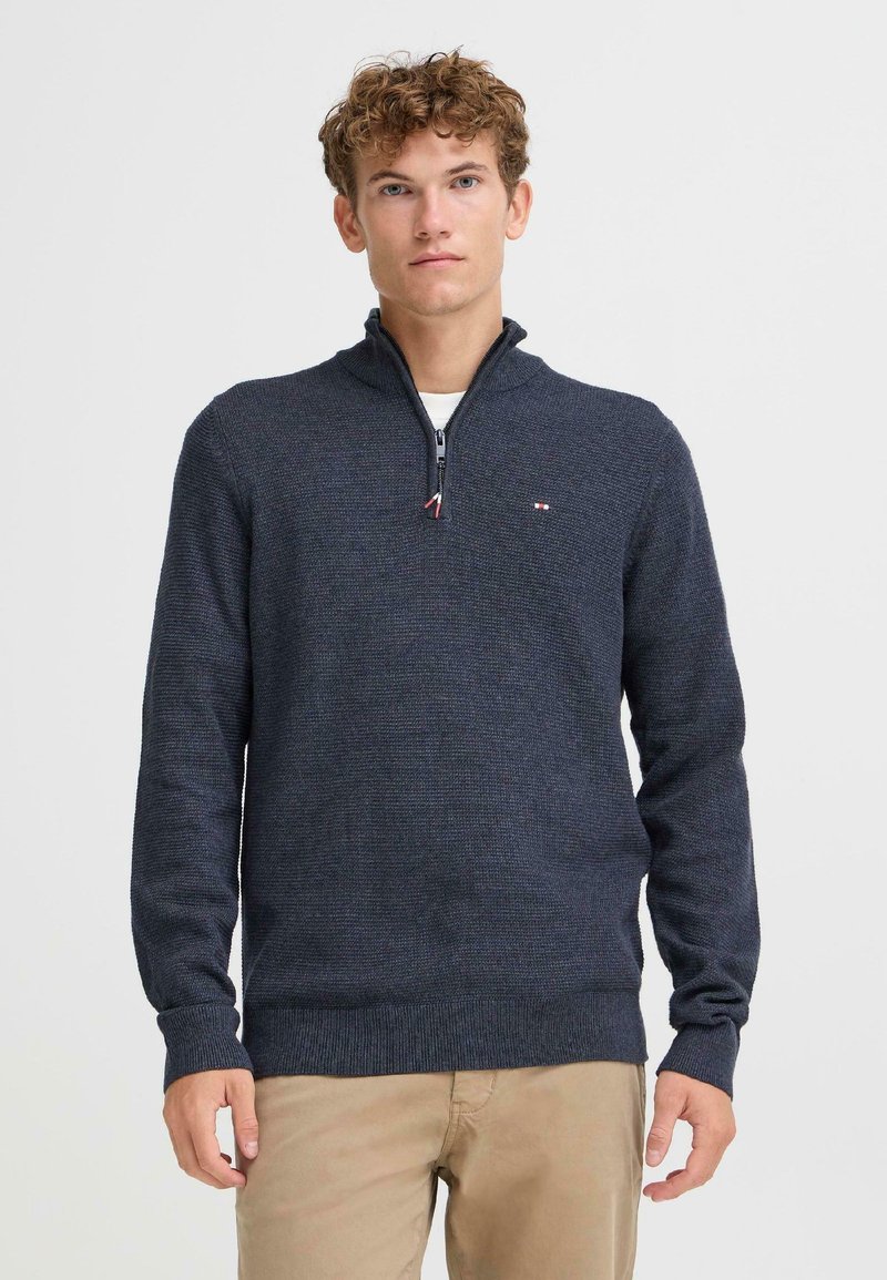 Sweater azul marino con cremallera y un tejido texturizado, con cuello alzado. Presenta mangas largas y un pequeño logo de la marca en el pecho.