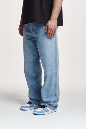 Helle blue, lockere Denim-Jeans, getragen mit weißen und hellblauen Turnschuhen. Die Textur ist glatt; das Design verfügt über einen klassischen Fünf-Taschen-Stil.