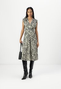 Robe à pois noirs et crème avec un design enroulé, décolleté en V et manches courtes. Assortie à des bottes noires arrivant au genou et un petit sac noir.