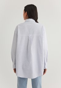 Light blue and white striped oversized shirt with long sleeves, a collar, back yoke detail, and button cuffs. Soft fabric texture.