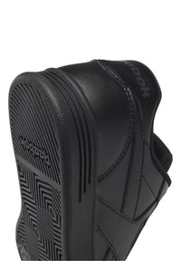 Svarta sneakers i slät läder. Har en texturerad gummisula med ett geometriskt mönster. Logotyp synlig på sidan.