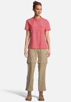 Camisa de cuadros rojos y blancos de manga corta con un bolsillo en el frente, combinada con pantalones cargo beige con cremallera y botas marrones con cordones.