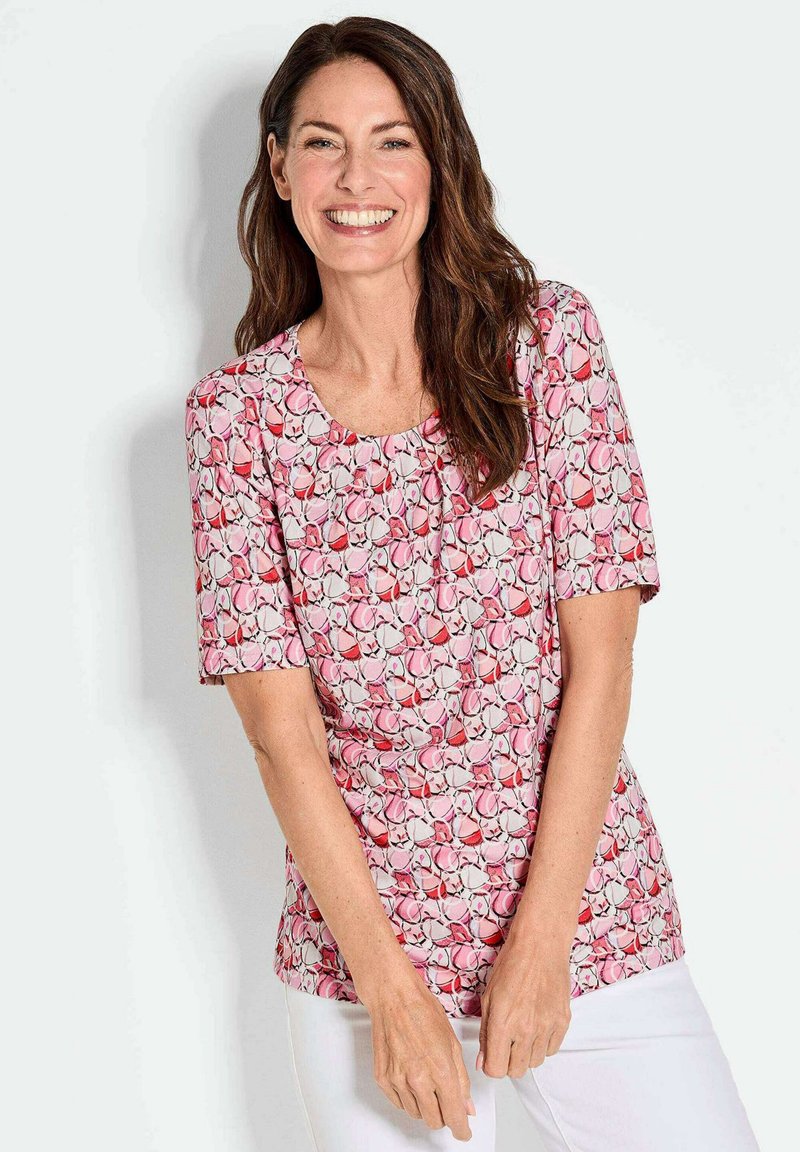 Kurzärmliges Oberteil mit einem pinken Blumenmuster und rundem Ausschnitt. Weicher Stoff mit einer figurbetonten Silhouette. Mit subtilen Details akzentuiert.