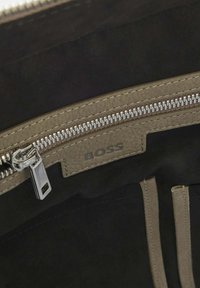 Black interior of a bag featuring a beige zippered pocket, silver zipper hardware, and a "BOSS" logo embossed on leather. Soft texture.