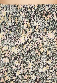 Tecido com padrão floral em fundo preto. Apresenta pequenas flores em amarelo pastel, rosa e verde, e uma cintura elástica com pregas.