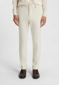 Beige broek met een rechte pijpdesign, met een platte voorkant, zijzakken en een knoopsluiting, gecombineerd met donkerbruine schoenen.