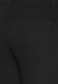 Černé džíny z denimu s hladkou texturou, vybavené jednou zadní kapsou a tónovým šitím. Design je přiléhavý a minimalistický.