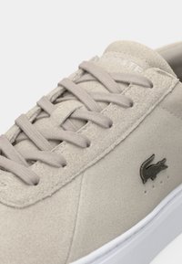 Μπεζ σουέντ αθλητικό παπούτσι με κορδόνια στο ίδιο χρώμα, λευκή σόλα και μαύρο κροκοδειλάκι στο πλάι.