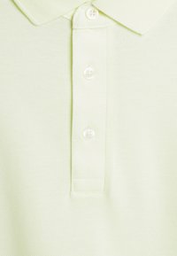 Světle zelené polo tričko s texturovanou tkaninou, tradičním límcem a třemi bílými knoflíky podél légy.