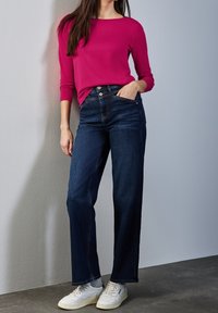 Fuksiankeltainen pitkähihainen paita yhdistetty tummansinisiin leveälahkeisiin farkkuihin. Rentoon asuun sopivat valkoiset tennarit. Yksinkertainen muotoilu, vähäiset yksityiskohdat.