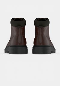 Braune Lederstiefel mit einem schwarzen elastischen Bund, runder Zehenform und strukturierter schwarzer Gummisohle mit horizontalen Rillen.