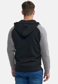 Sudadera con capucha de cuerpo negro y mangas raglán grises. Está hecha de un tejido suave, incluye un bolsillo frontal y puños acanalados.