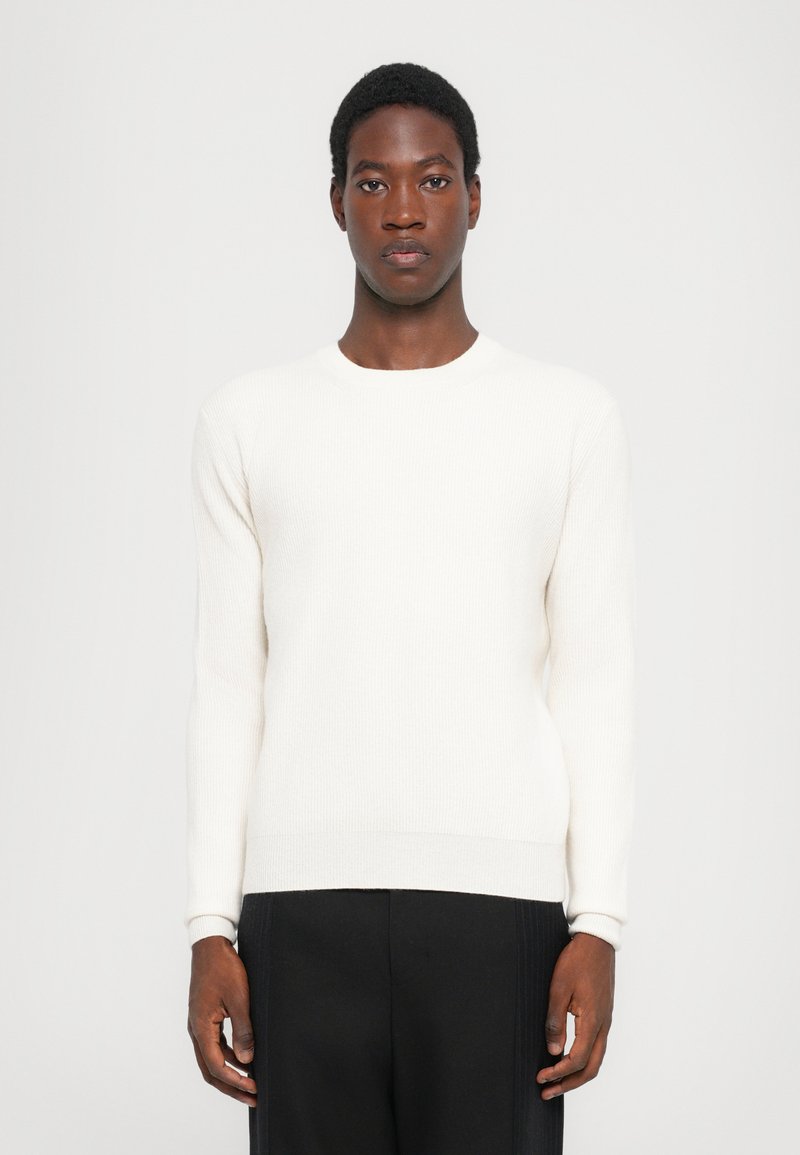 White ribbed long-sleeve sweater with a round neckline, featuring a fitted silhouette and soft texture. Paired with black wide-leg trousers.