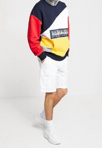 Mørkeblå, rød, hvid og gul farveblokket pullover med en quarter-zip design og logo patch, parret med hvide cargo shorts og sneakers.