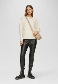 Hellbeige gerippter Pullover, schwarze Kunstlederleggings und schwarze Knöchelstiefel. Braune Umhängetasche mit einem einzigen Riemen.