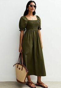 Olijfgroene midi-jurk met puffmouwen, vierkante halslijn en smock-bodice. G gedragen met bruine sandalen en een twee-kleurige handtas.
