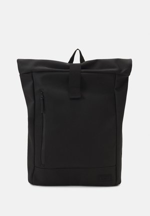Sac à dos noir à rabat, fabriqué en tissu durable, avec une poche zippée à l'avant, une poignée en boucle en haut et une base plate pour la stabilité.