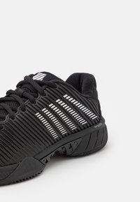 Černá sportovní obuv s pruhovanými stříbrnými akcenty, strukturovaným povrchem a odolnou gumovou podrážkou. Šněrovací design s vyztuženou oporou paty.