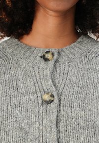 Gray knitted cardigan with a round neckline, featuring two dark buttons. The texture is thick and ribbed, indicating warmth and comfort.