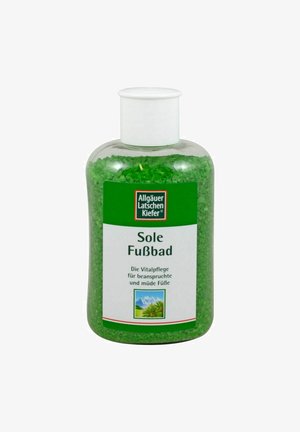 Grüne Badezusätze in einer durchsichtigen Plastikflasche mit einem weißen Deckel. Das Etikett zeigt Text sowie ein Bild von Bergen und Grünflächen.