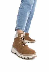 Stivaletti alla caviglia in suede marrone con una suola intermedia bianca, lacci grigi e un colletto testurizzato. Presentano una zip laterale e suola robusta per una migliore aderenza.