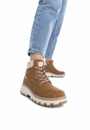 Stivaletti alla caviglia in suede marrone con una suola intermedia bianca, lacci grigi e un colletto testurizzato. Presentano una zip laterale e suola robusta per una migliore aderenza.