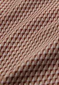 Textiel met een herhalend ruitpatroon in bruin en lichtbeige, met een zachte, gebreide textuur. De stof lijkt licht uitgerekt.