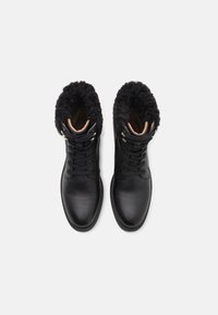 Pair of black leather winter boots with thick black fur lining, laces, and metal eyelets, viewed from above on white background.