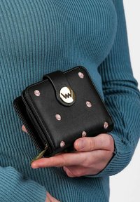 Černá kožená peněženka s růžovými puntíky, zlatými detaily a bezpečným uzávěrem. Design zahrnuje zipovou přihrádku a kompaktní tvar.